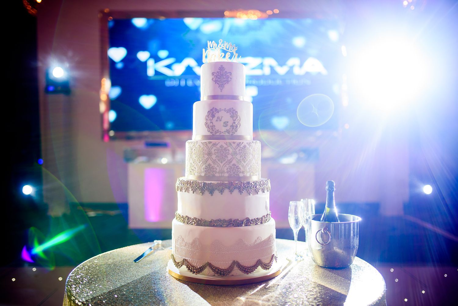 Elegant tiered wedding cake displayed with dramatic blue lighting at reception venue.