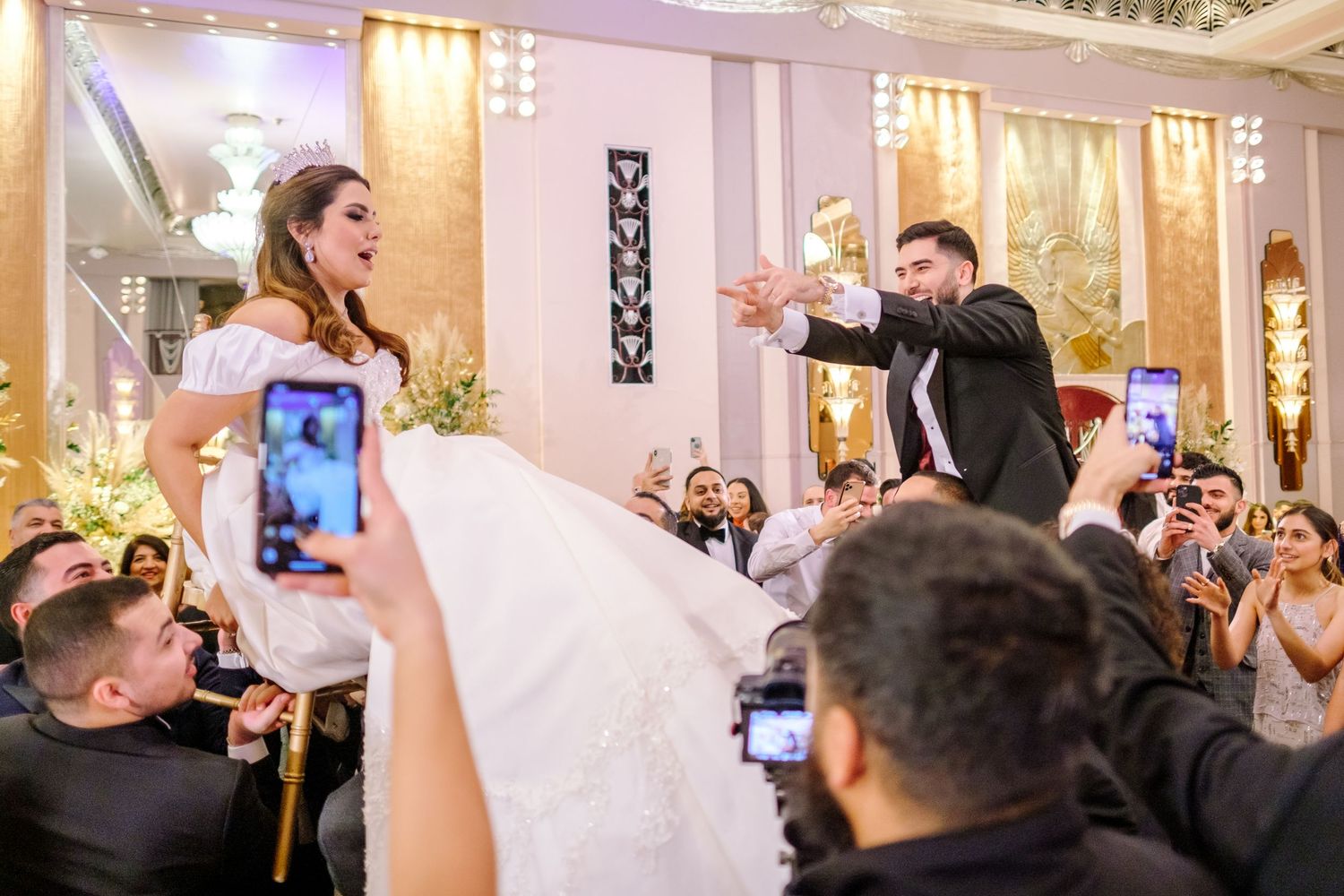 Celebration in a grand ballroom with guests cheering and raising their hands in joy.