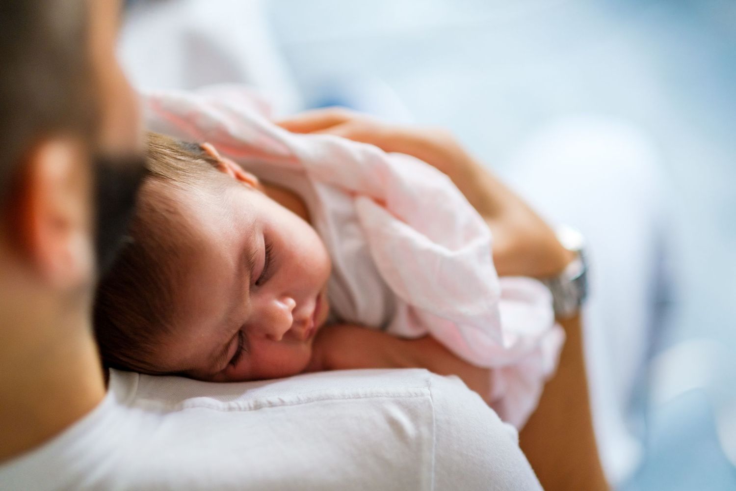 A sleeping newborn baby wrapped in white blankets rests peacefully.