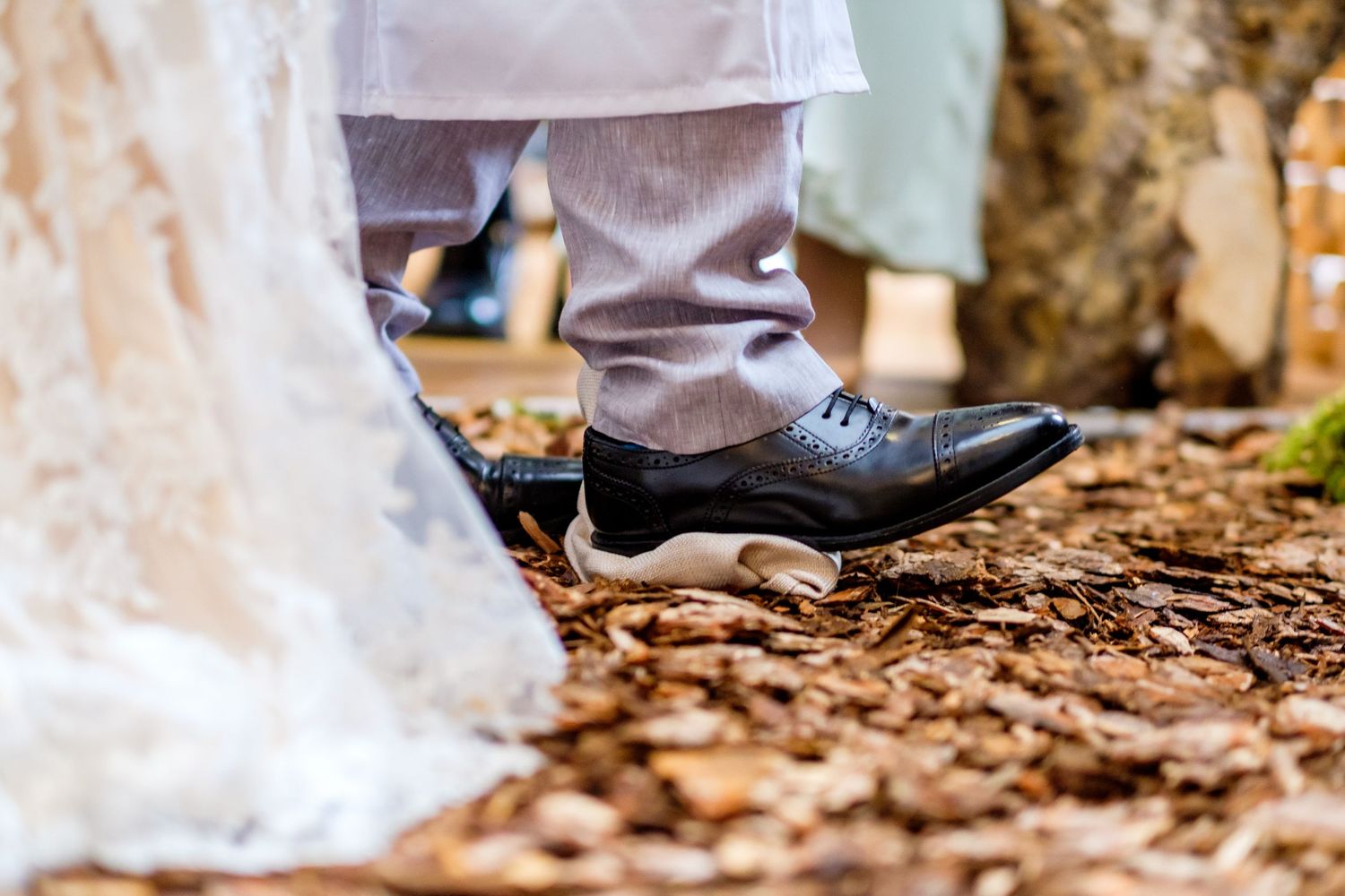 Close-up shot of formal shoes and wedding dress hem on brown autumn leaves.