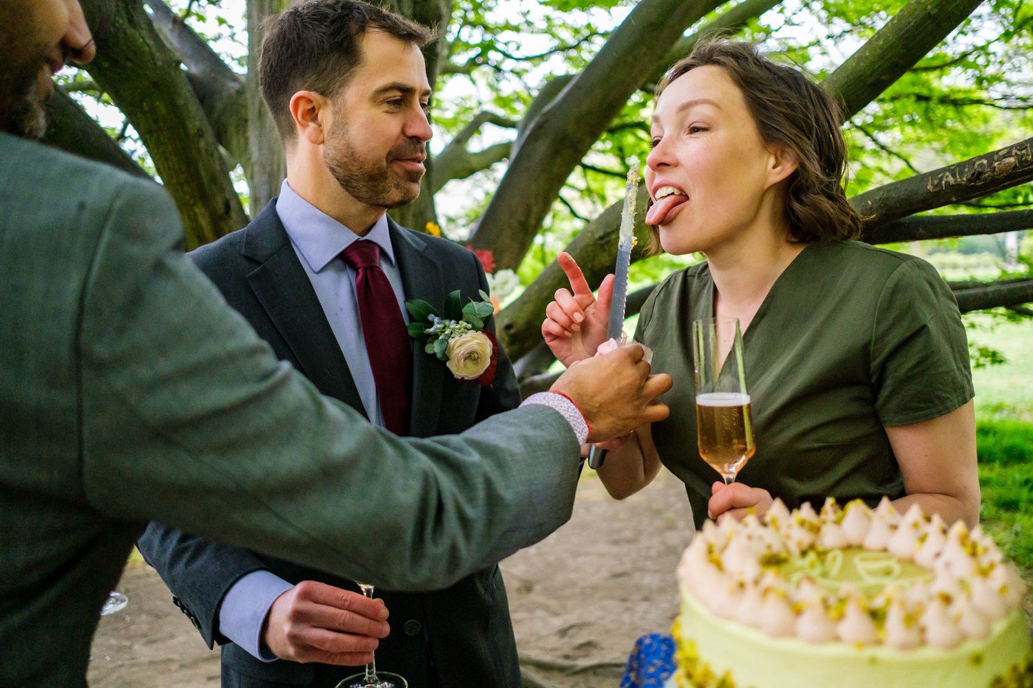 A couple shares cake and champagne while sitting together outdoors under green foliage.