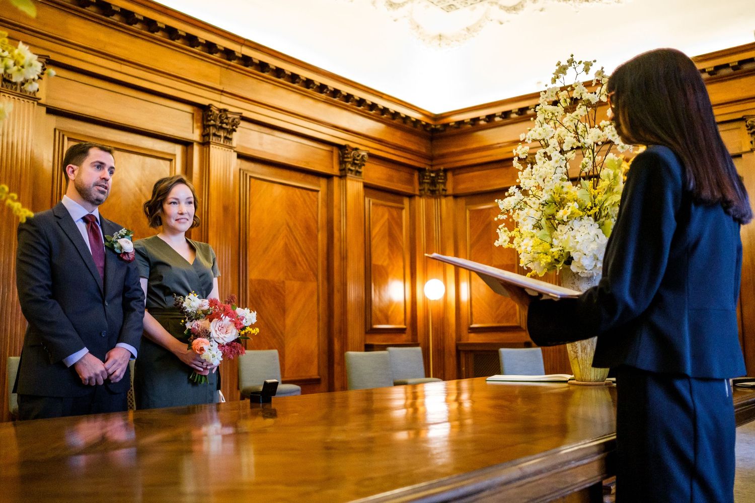 A luxurious wood-paneled ceremony space with ornate moldings and chandeliers during an indoor wedding celebration.