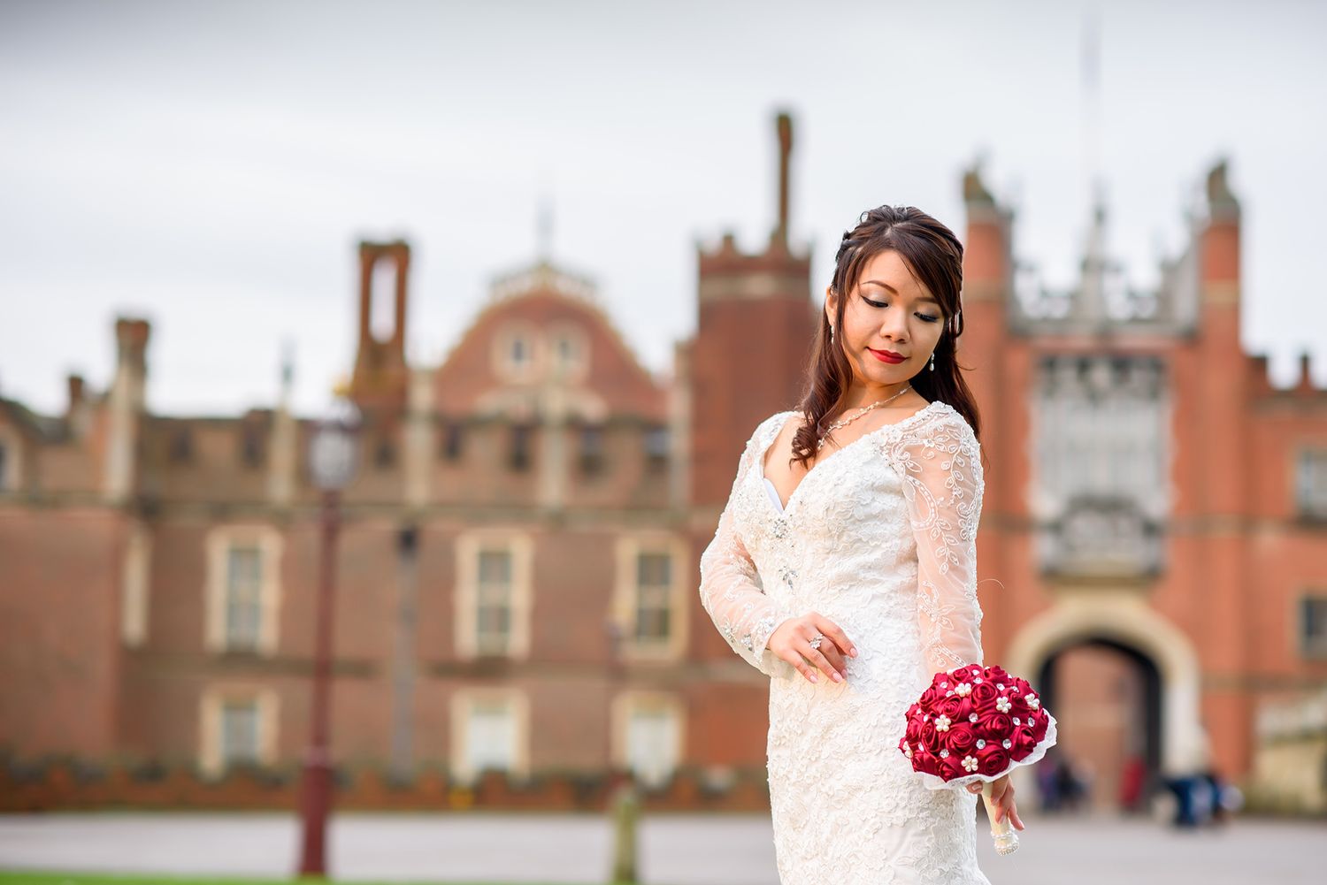 Elegant bride in white lace dress posing outside historic brick architecture.