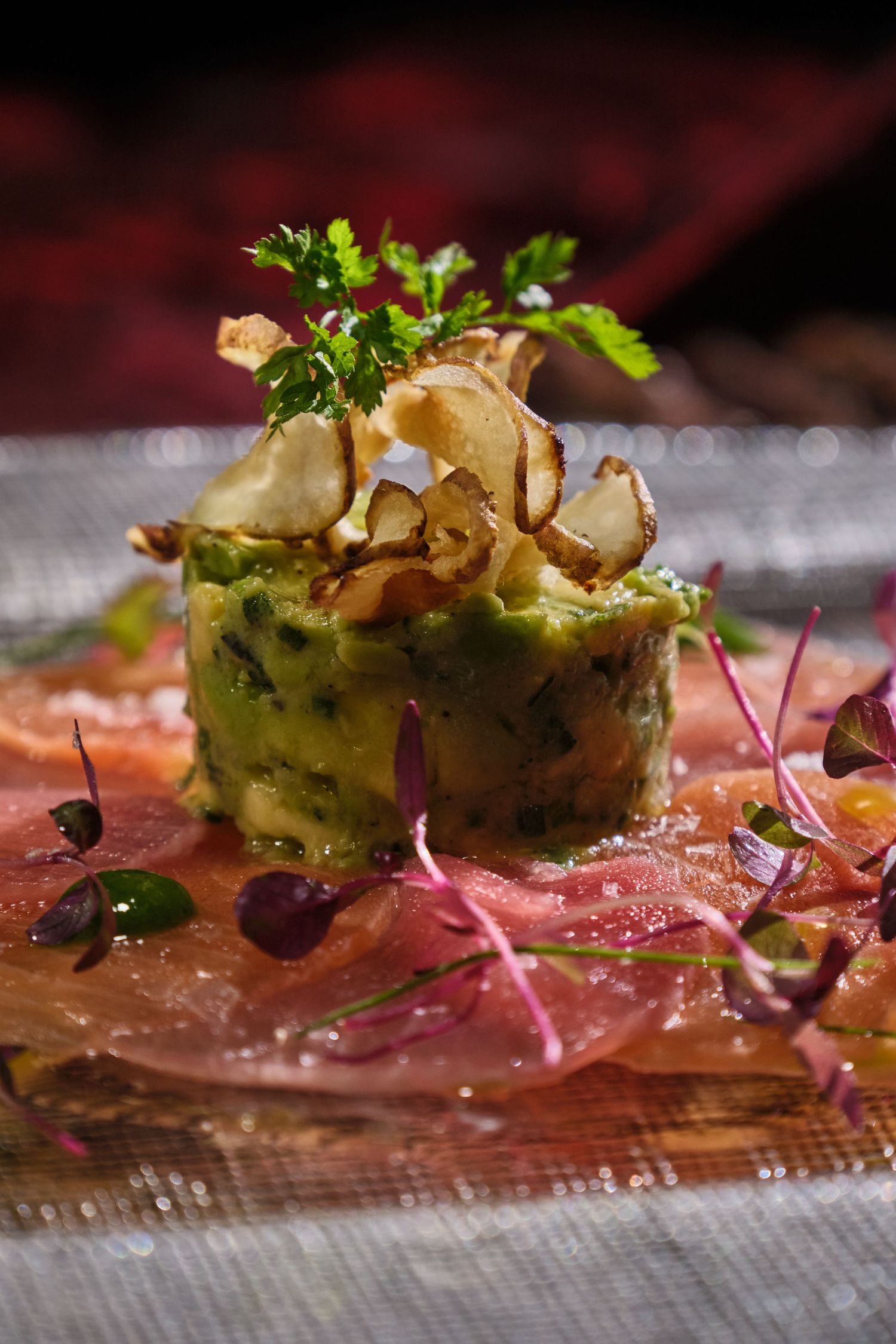Elegant salmon tartare with avocado, crispy chips, and microgreens on a wooden board, fine dining presentation.