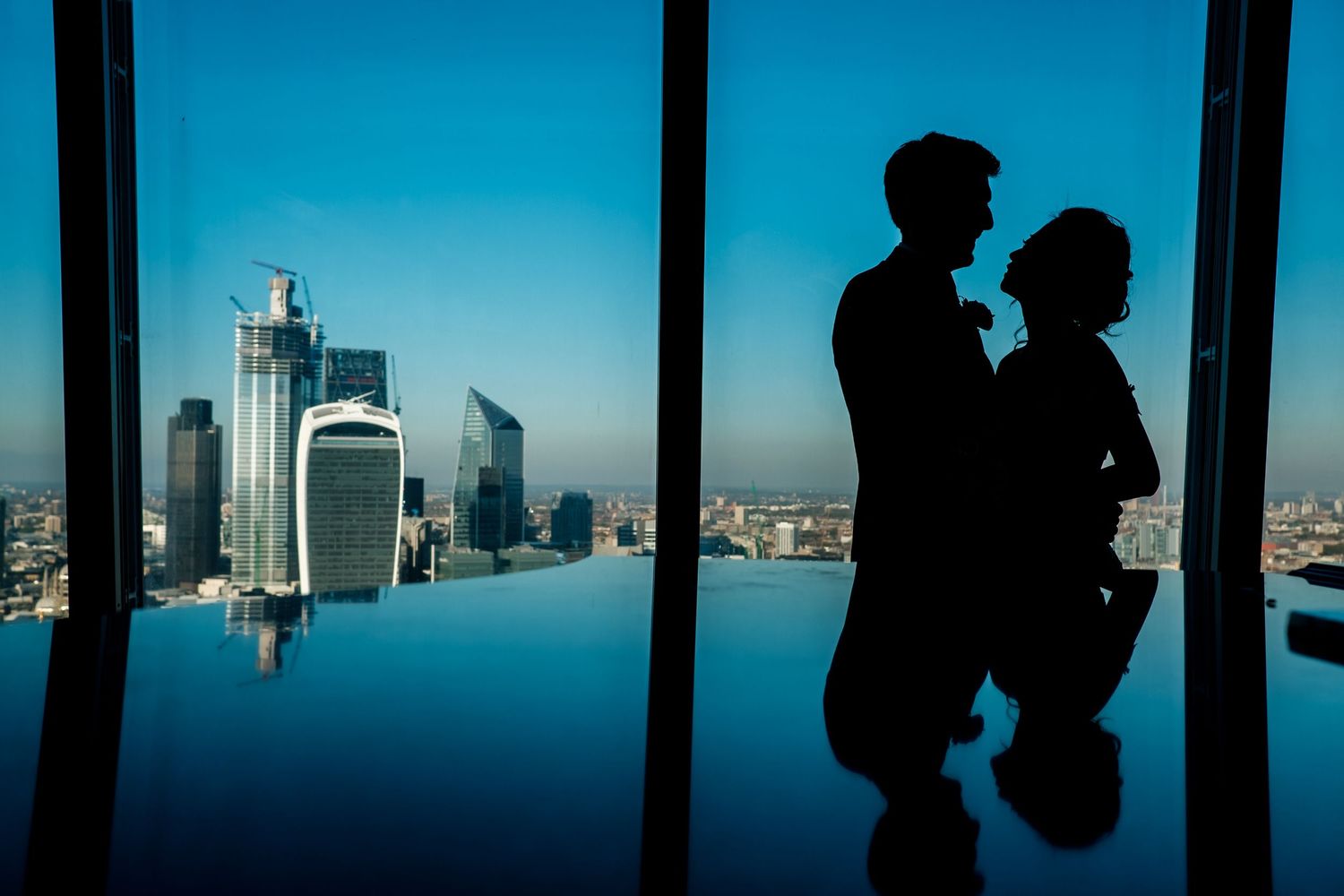 Silhouettes against large windows with a cityscape view and bright blue sky.