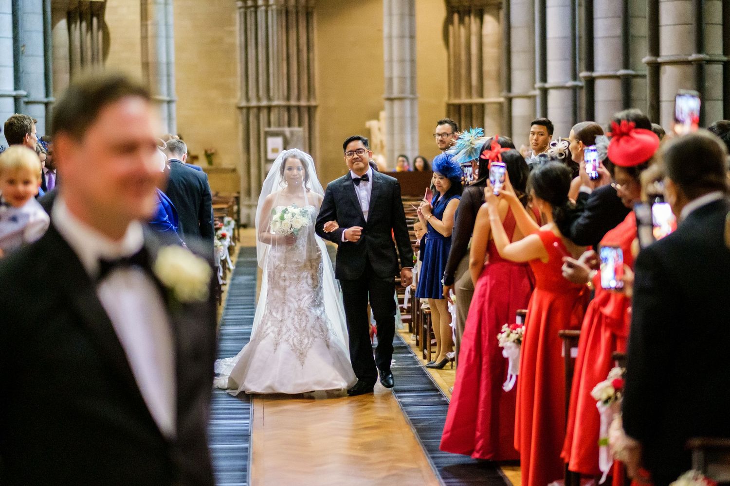 Wedding ceremony in a grand cathedral with red-robed choir members lining the aisle.