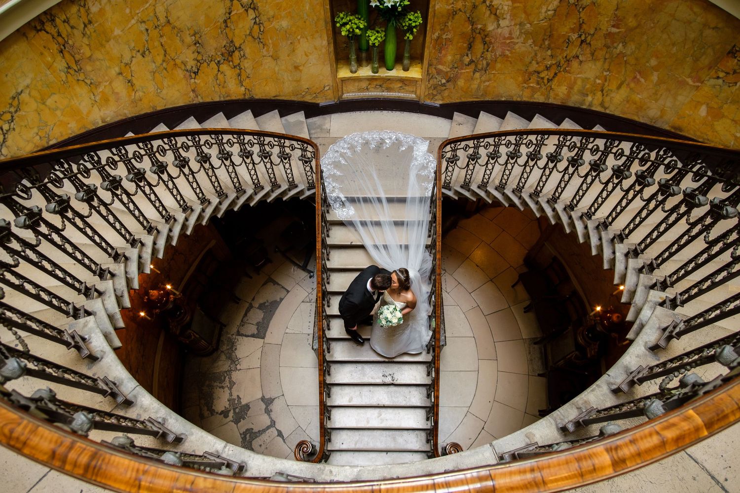Aerial view of an elegant spiral staircase with ornate wrought iron railings in a historic building.