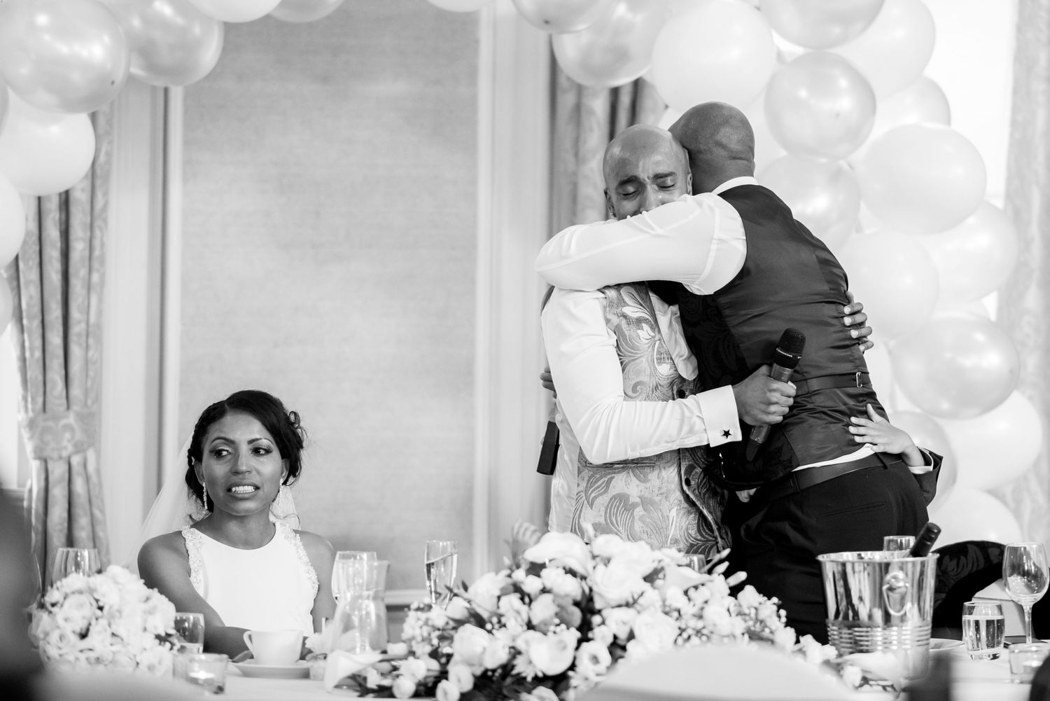 Black and white photograph of wedding guests embracing and dancing at a reception celebration.