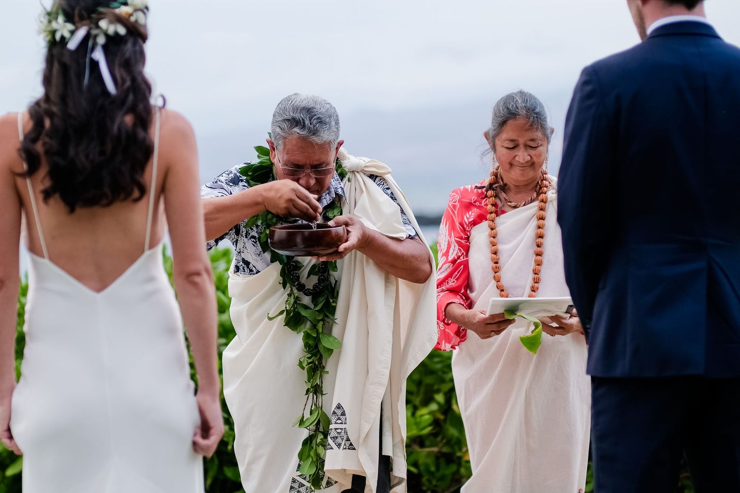 Wedding ceremony participants lined up outdoors in white dresses and dark suits.