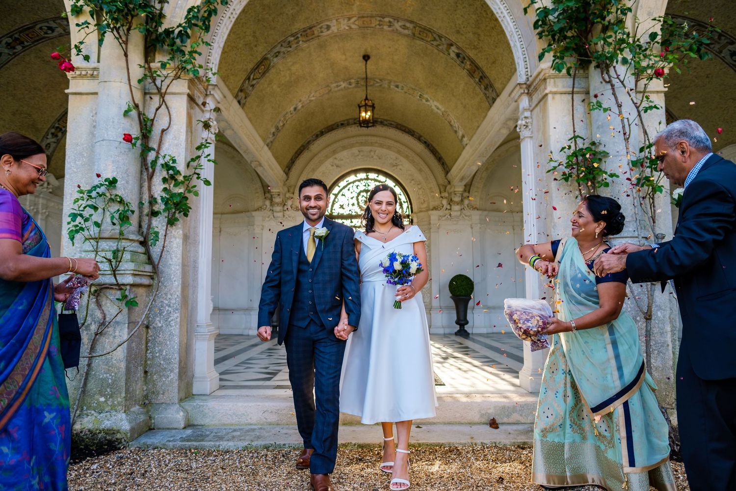 Romantic ceremony setting under stone archways decorated with greenery and natural light.