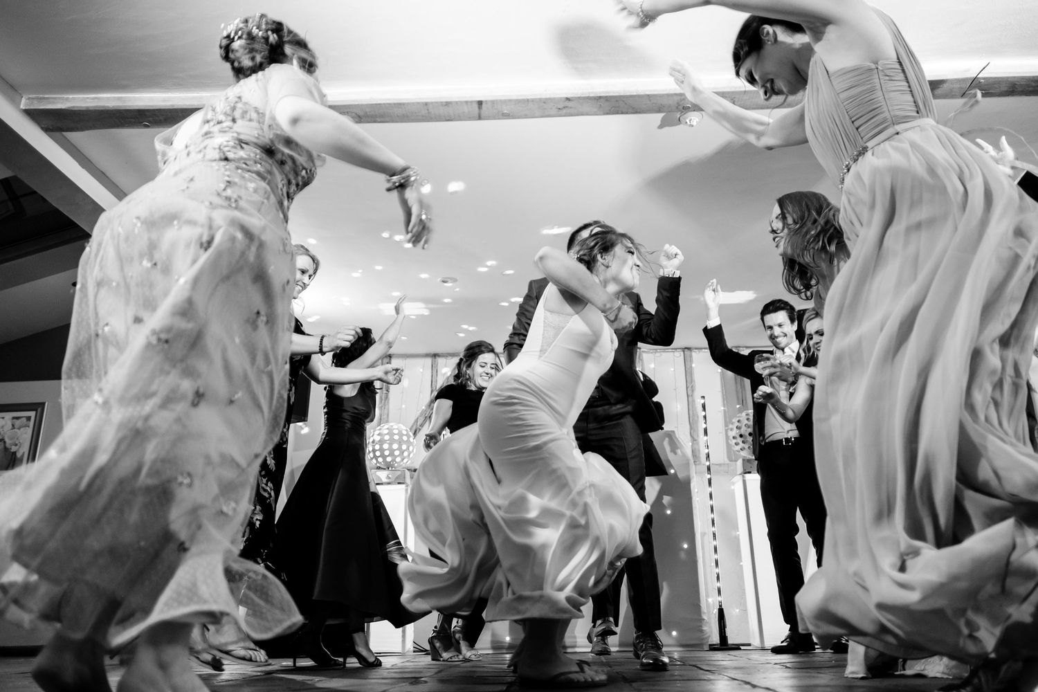 Black and white photo of wedding guests dancing and twirling their dresses on the dance floor.