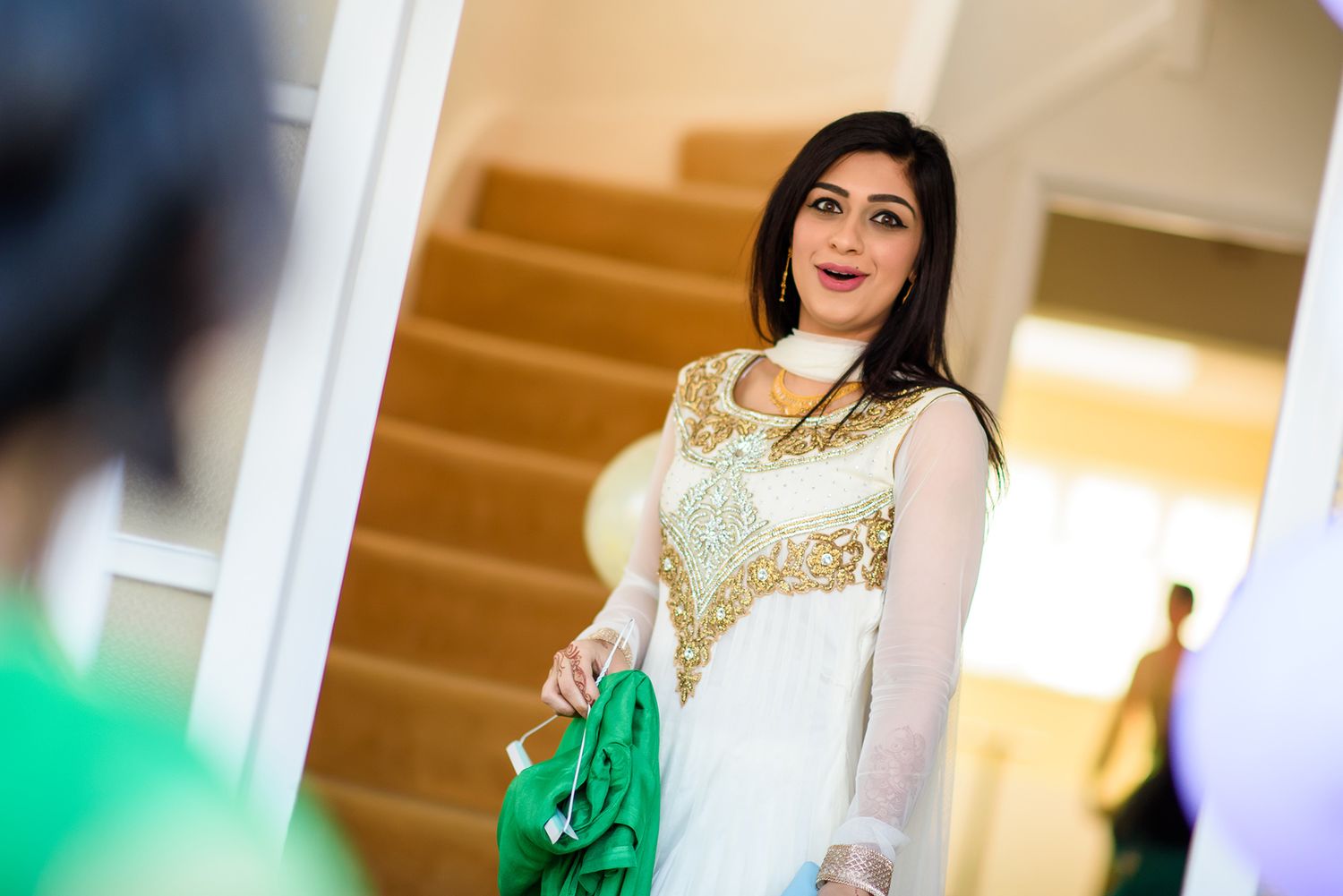 An elegant woman in traditional white and gold attire smiles during a celebration.