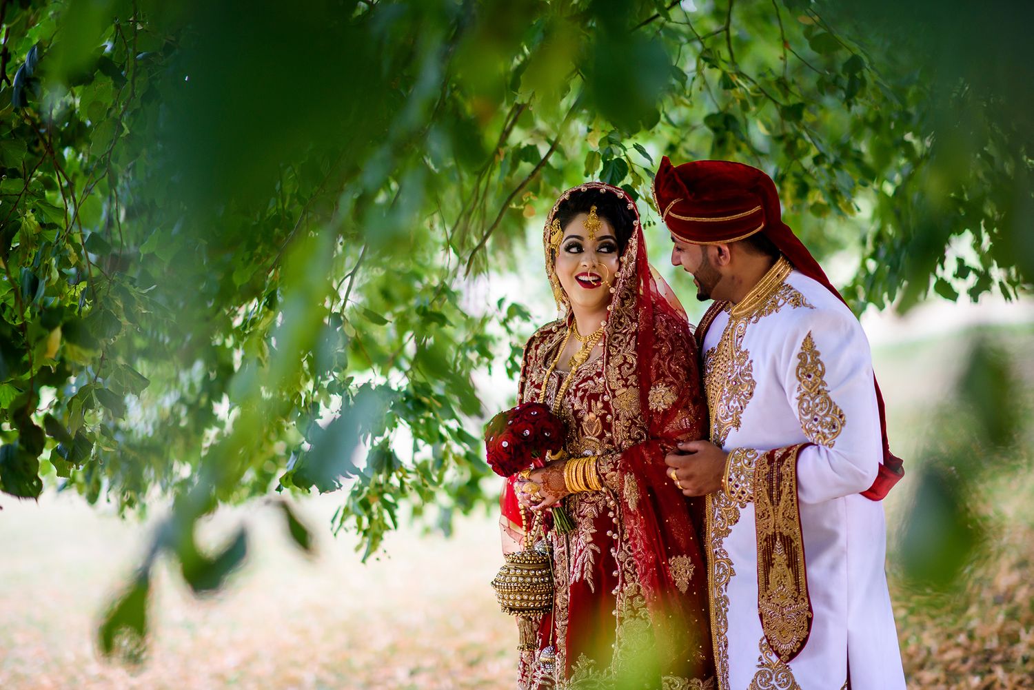 Romantic wedding portrait beneath green tree canopy with traditional Indian outfits.