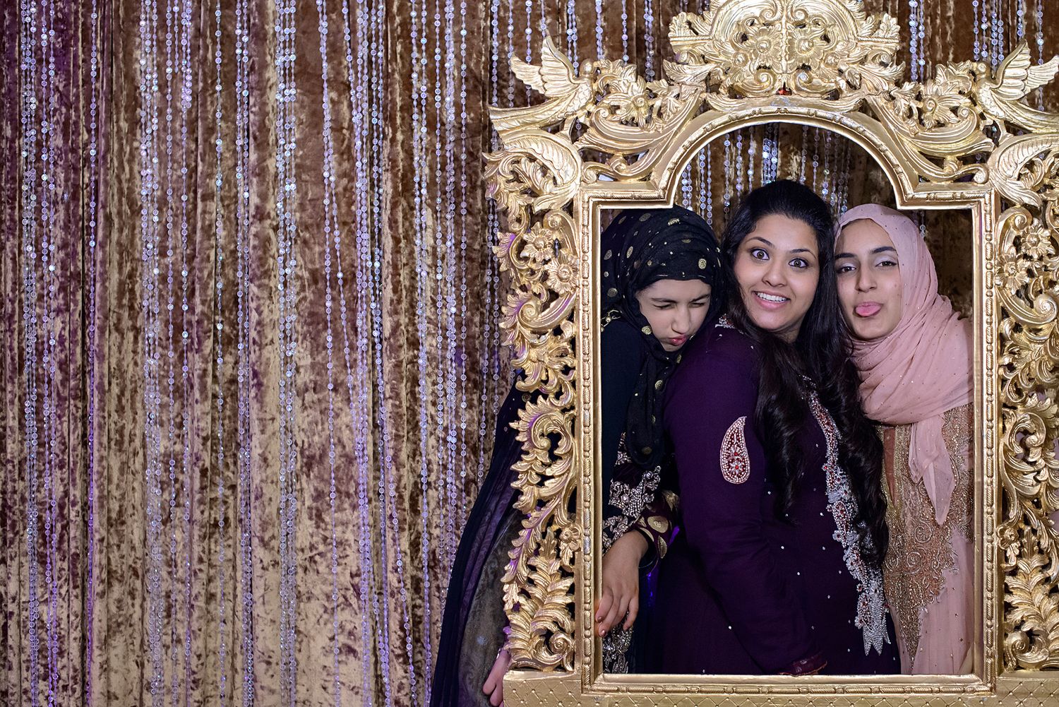 Wedding guests pose against decorative backdrop with ornate gold frame details.