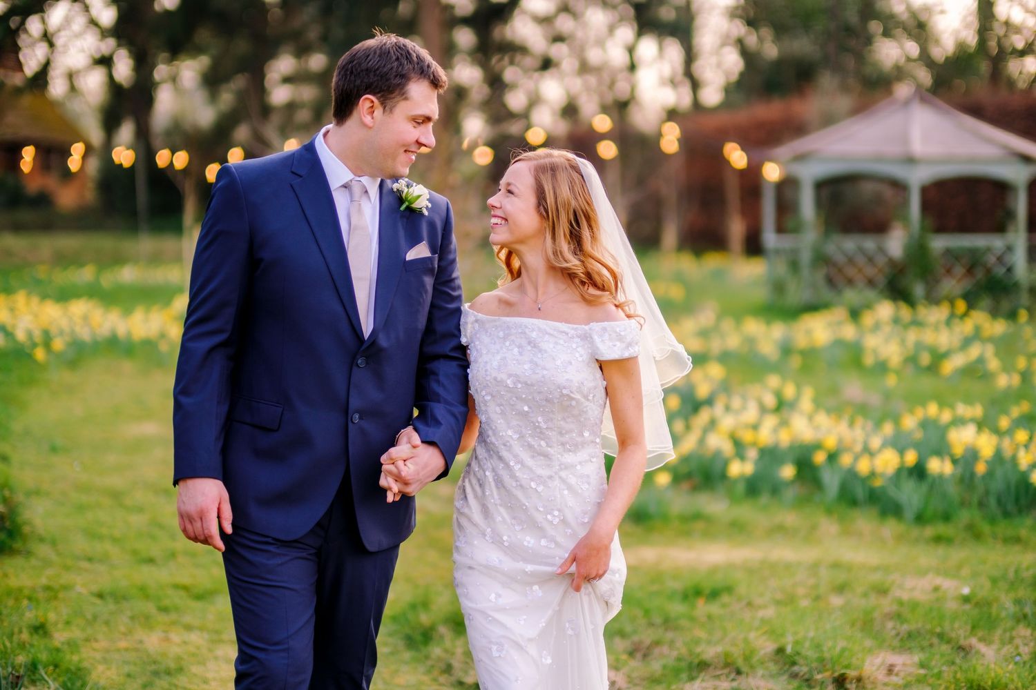 A joyful wedding couple shares a laugh while walking through a spring garden filled with daffodils.