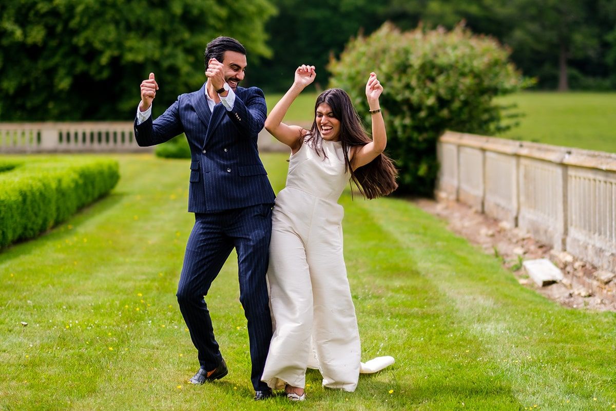 Celebratory dance moves on a manicured garden path by couple in wedding attire.