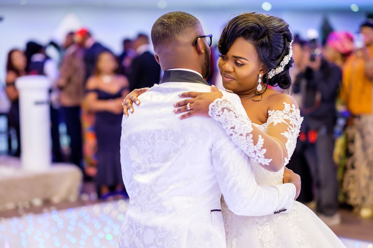 A formal celebration dance with guests wearing elegant white attire on a crowded dance floor.