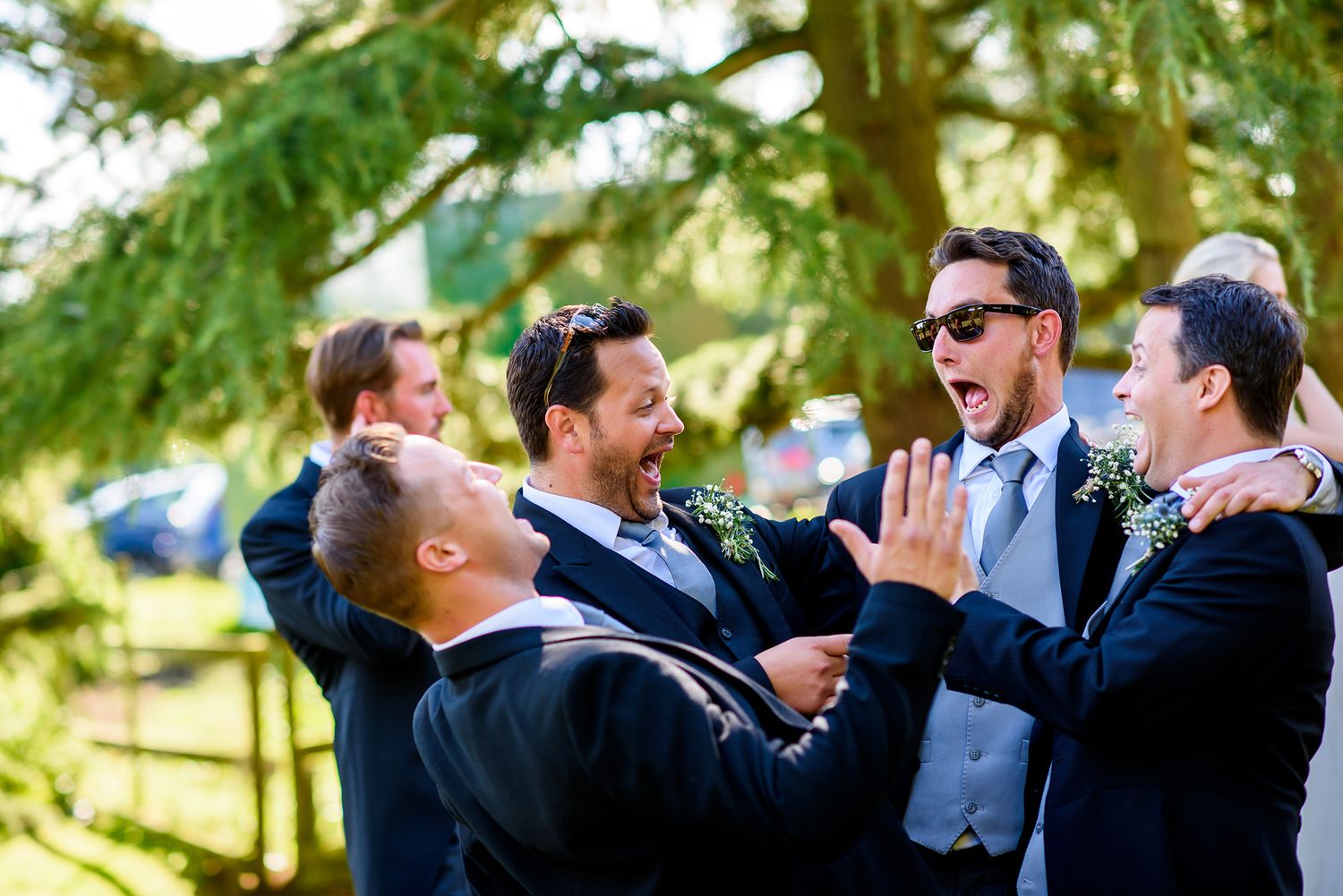 Wedding party members sharing joyful moments and laughter together outdoors on a sunny day.