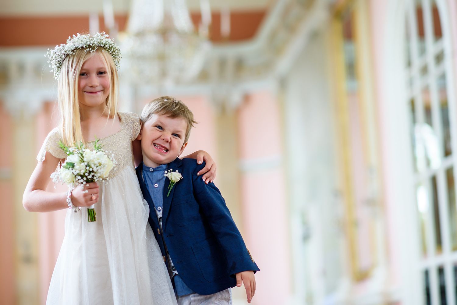 Young wedding attendants in formal attire posing together with flowers and crowns.
