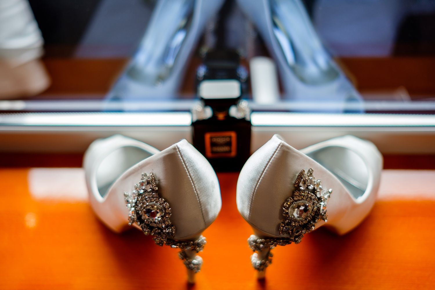 Elegant white bridal shoes with crystal embellishments displayed on an orange surface.