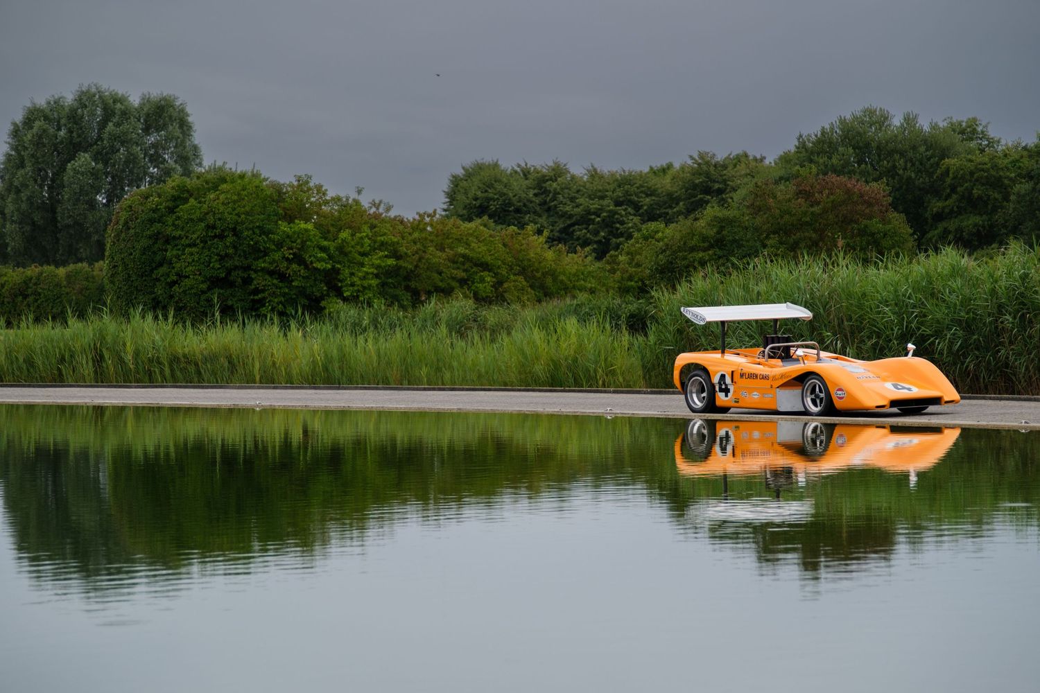 Serene lake landscape with orange seaplane floating on calm waters near reed-lined shore.