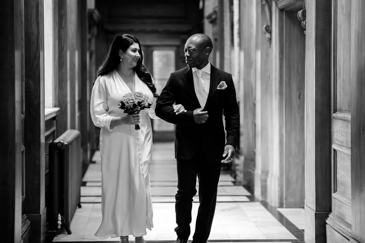 Couple walking through an elegant marble hallway with classical architectural details.