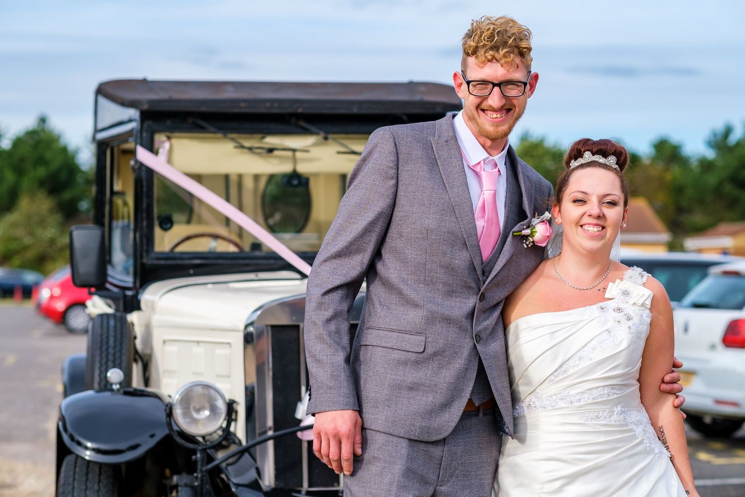 Wedding couple posing near vintage cars during outdoor summer photo session.