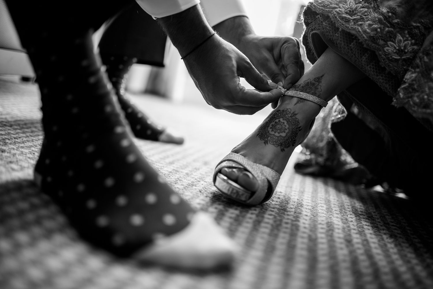 Close-up black and white detail shot of hands and feet on a patterned carpet.