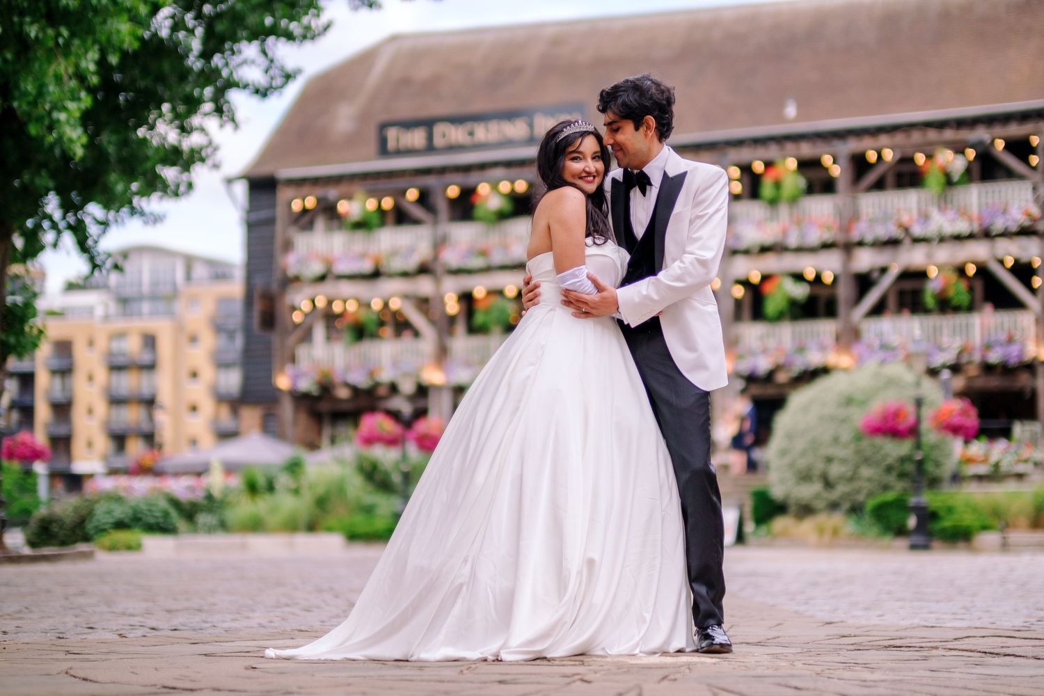 Newlyweds share an intimate dance pose in front of a flower-adorned building.