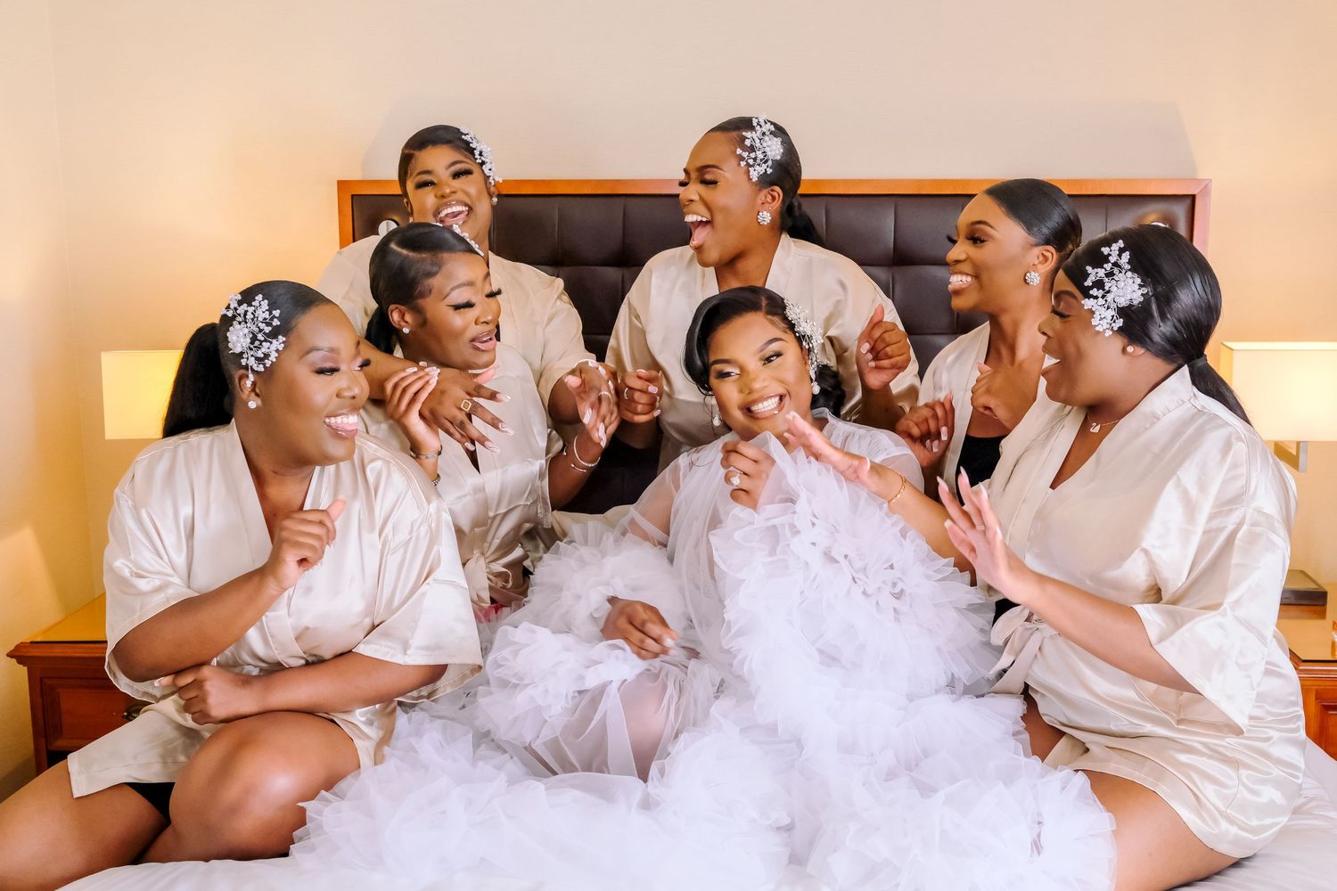 Wedding party members share joyful laughter and embraces while wearing white outfits.