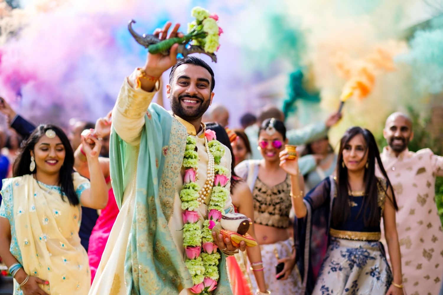 Festive celebration at Indian wedding with colorful powder and garlands amid joyful dancing and vibrant atmosphere.