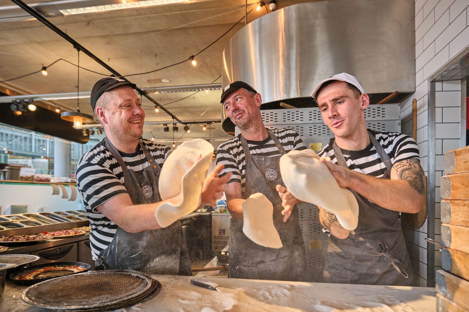 Pizza makers showing off freshly tossed dough in a professional kitchen.
