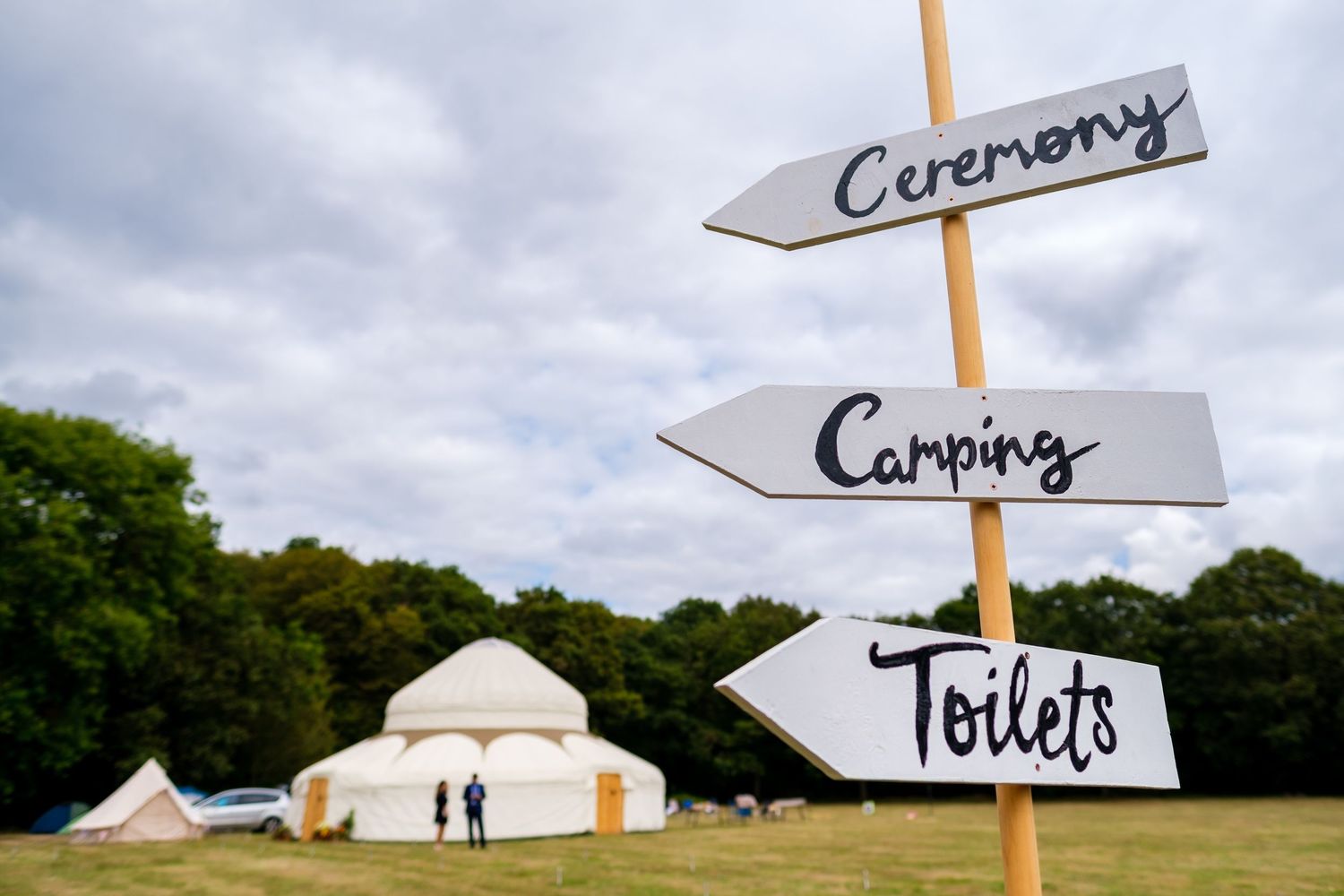 Directional signs point to ceremony, camping, and toilets against cloudy sky.