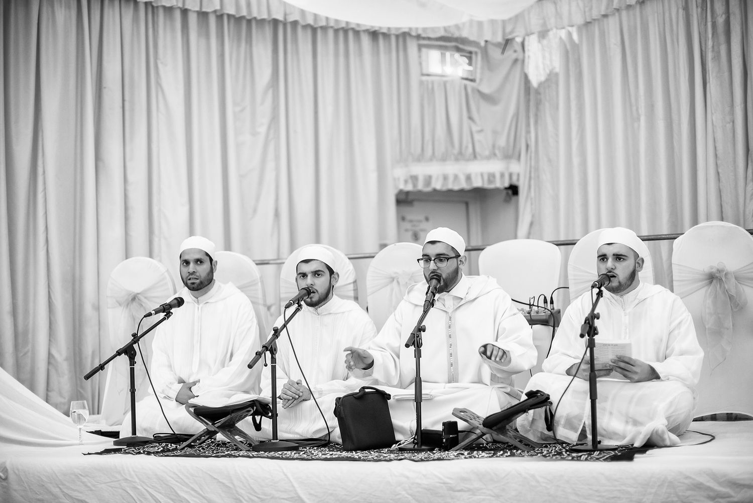 Musicians in white robes perform traditional music while seated on the floor.