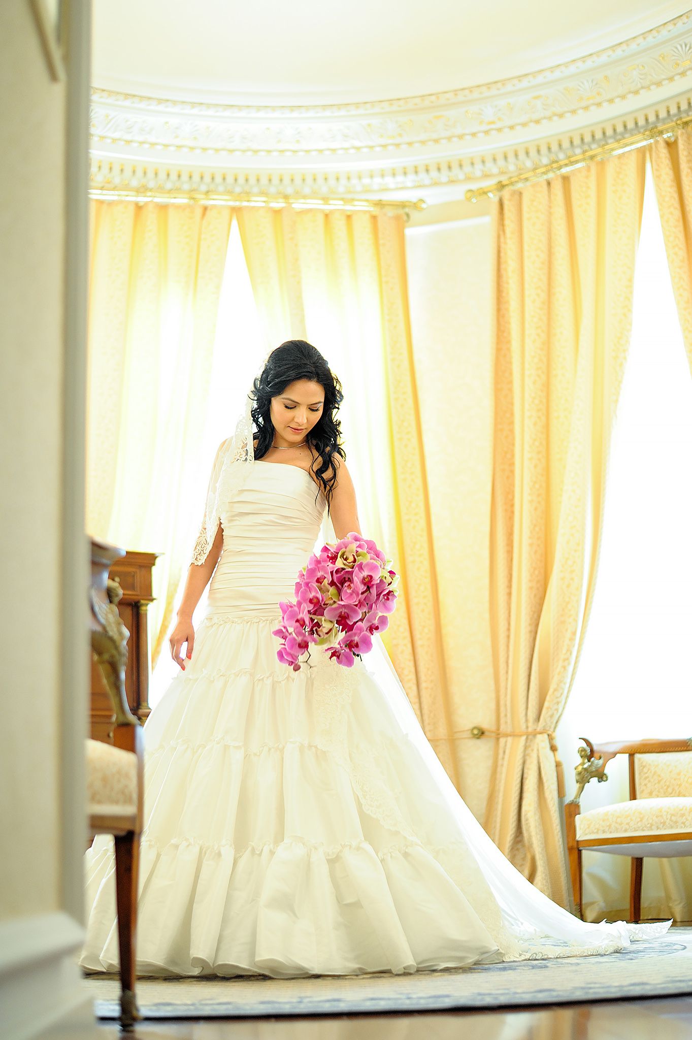 An elegant bridal portrait in a cream gown holding pink orchids.