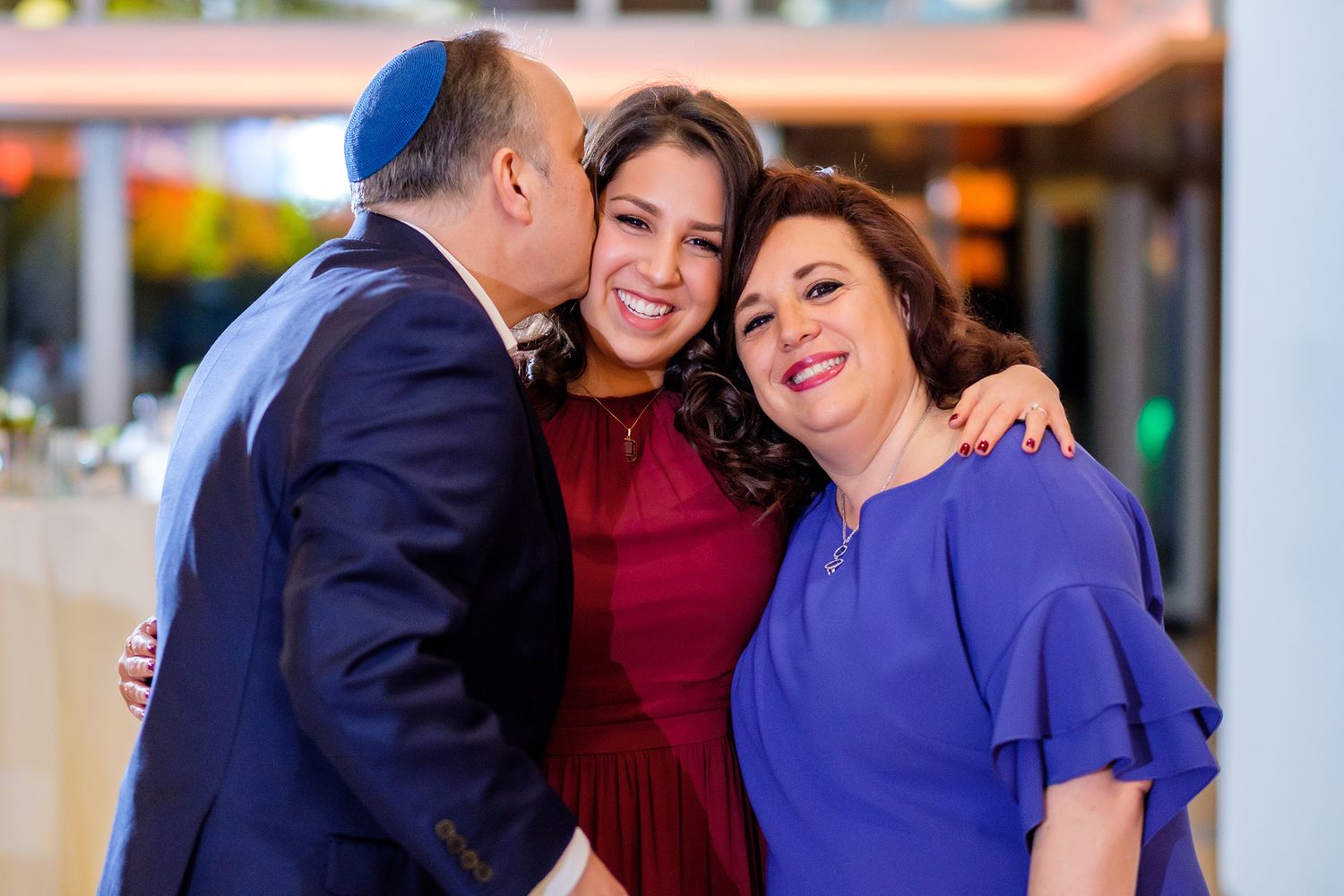Small group dressed in formal attire embracing and smiling together.
