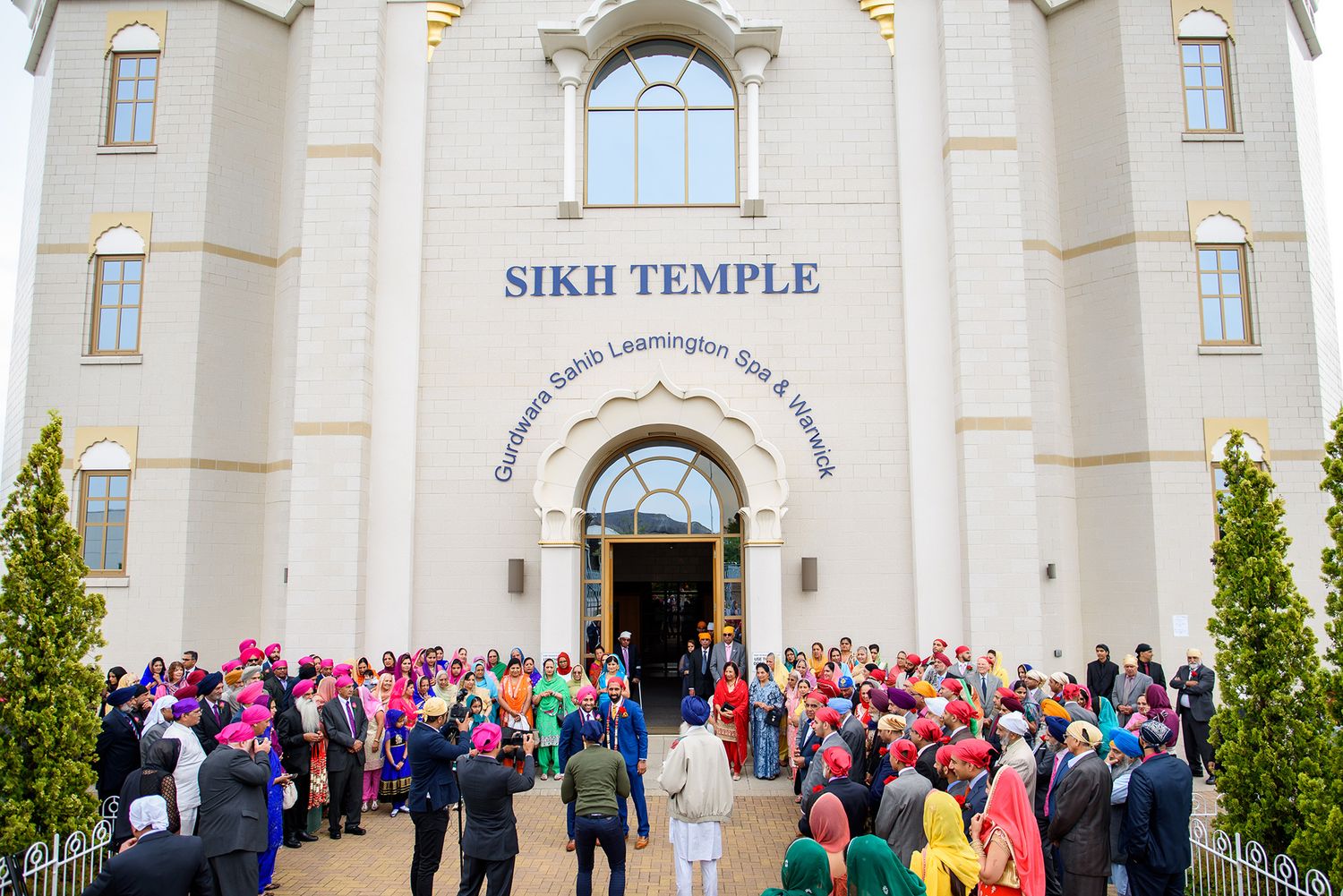 Large crowd gathered outside a white Sikh temple for a ceremony.