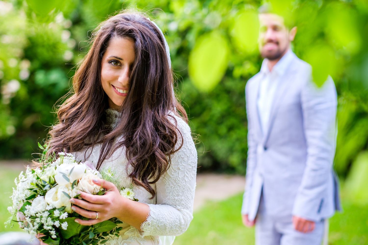 Wedding party poses together in a lush green garden setting during summer celebration.