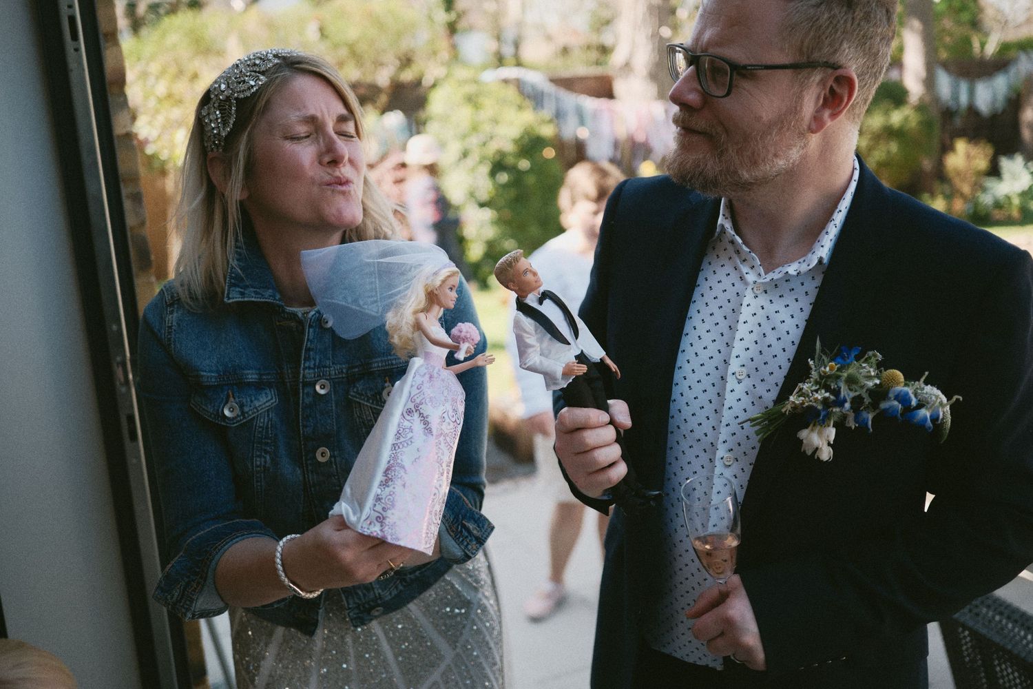 Wedding guests share drinks and laughter in a sunny outdoor garden setting.