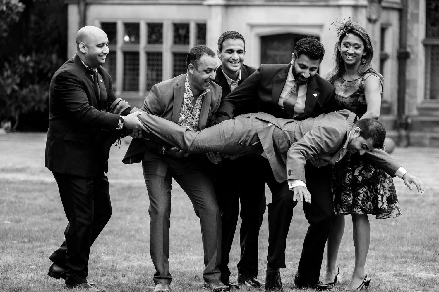 Wedding party strikes fun poses together on lawn in front of classic architecture.