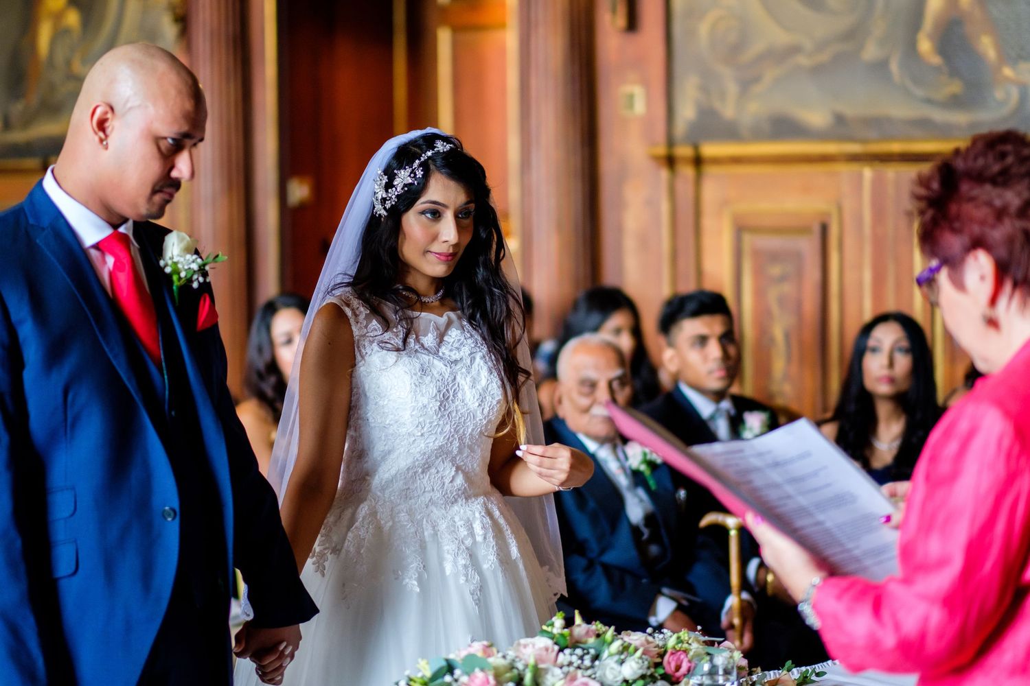 Wedding celebration with guests and couple in a richly decorated historic venue.