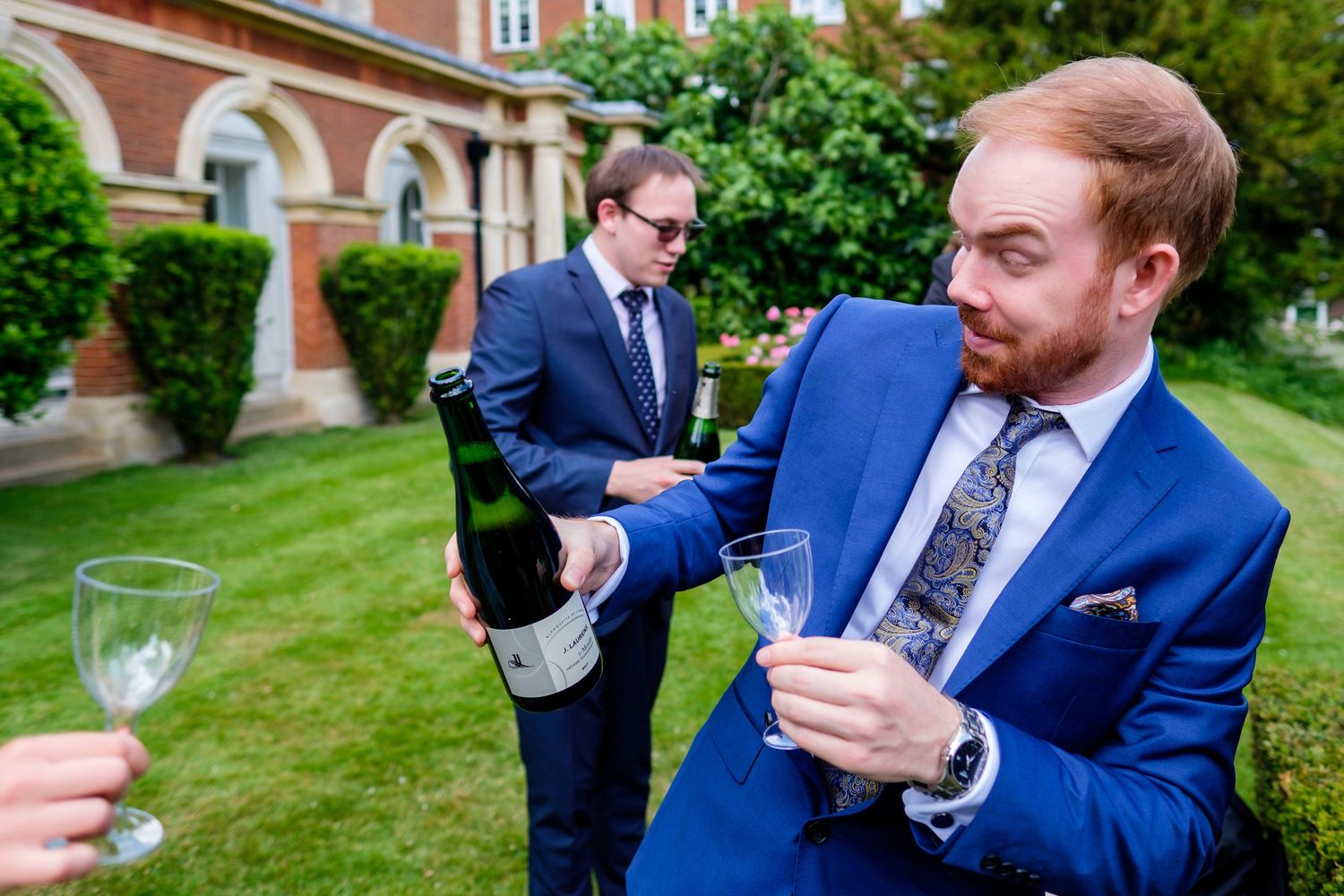 Wedding guests enjoy drinks and conversation at an outdoor garden reception.
