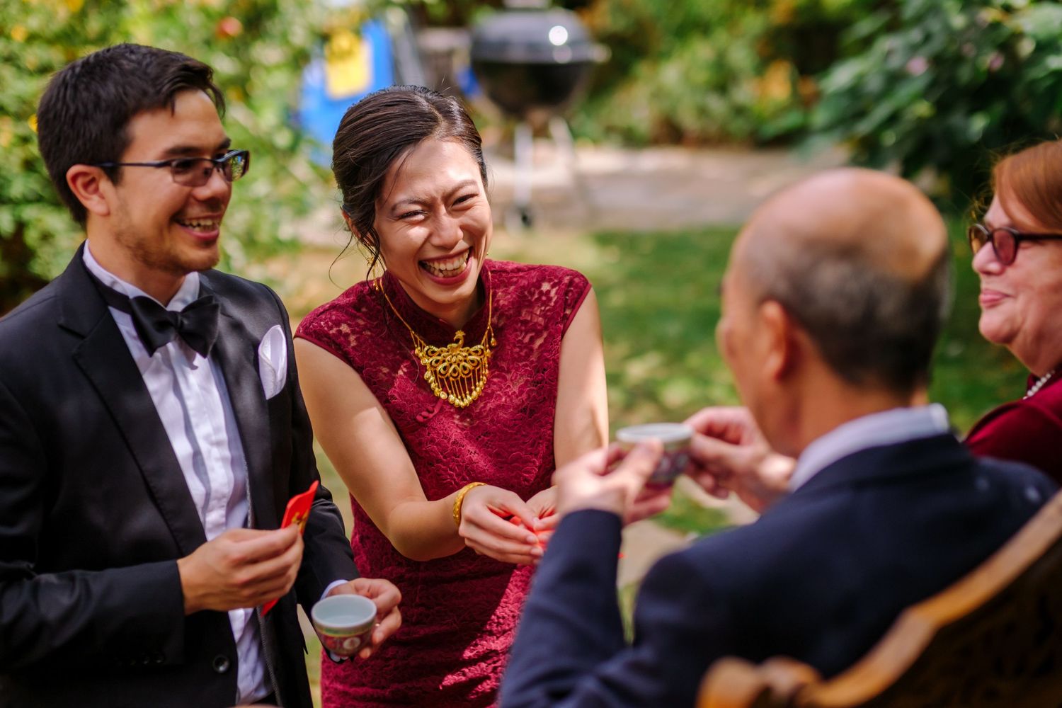 Wedding guests enjoying outdoor cocktail reception with drinks and laughter in garden setting.