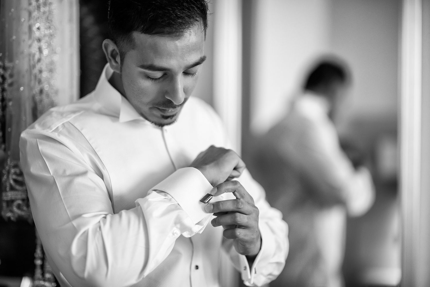 Person adjusting cufflinks on crisp white formal shirt in black and white photo.