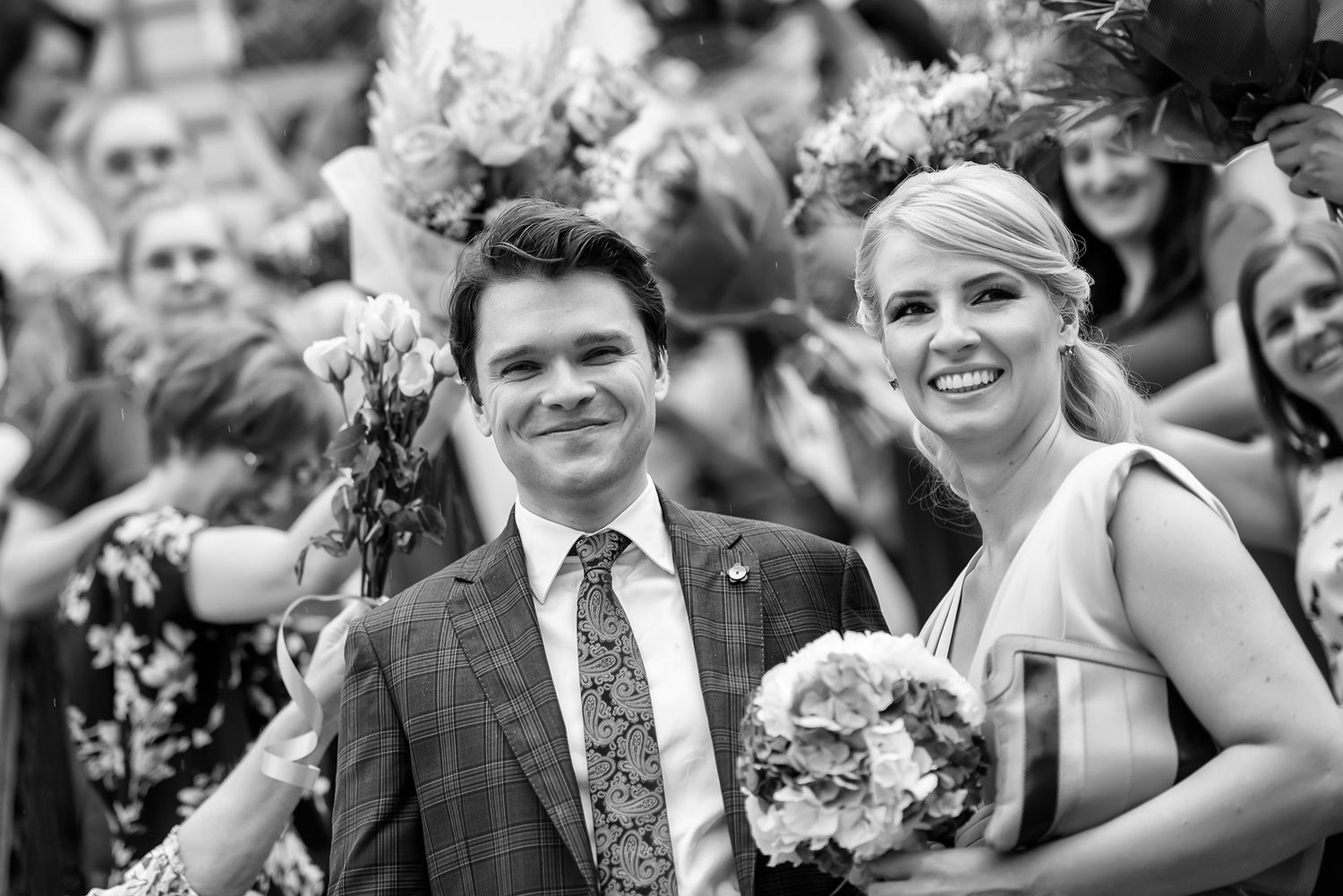 Black and white wedding party photo with bridesmaids and groomsmen smiling together.