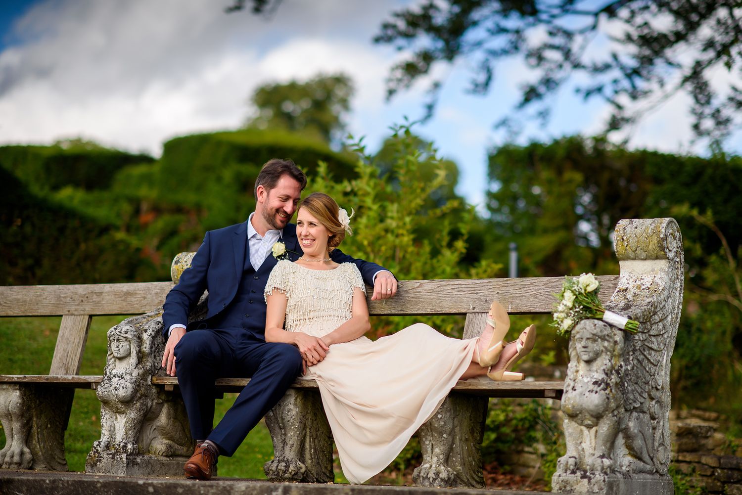 Romantic couple portrait on decorative stone bench surrounded by lush gardens.