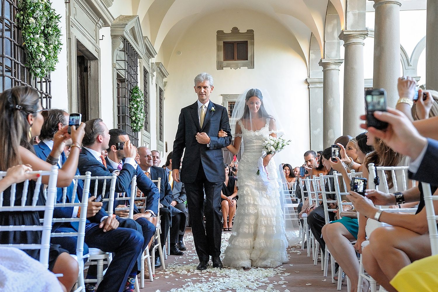 Wedding guests line a beautiful archway corridor, creating a celebratory tunnel for the newlyweds.