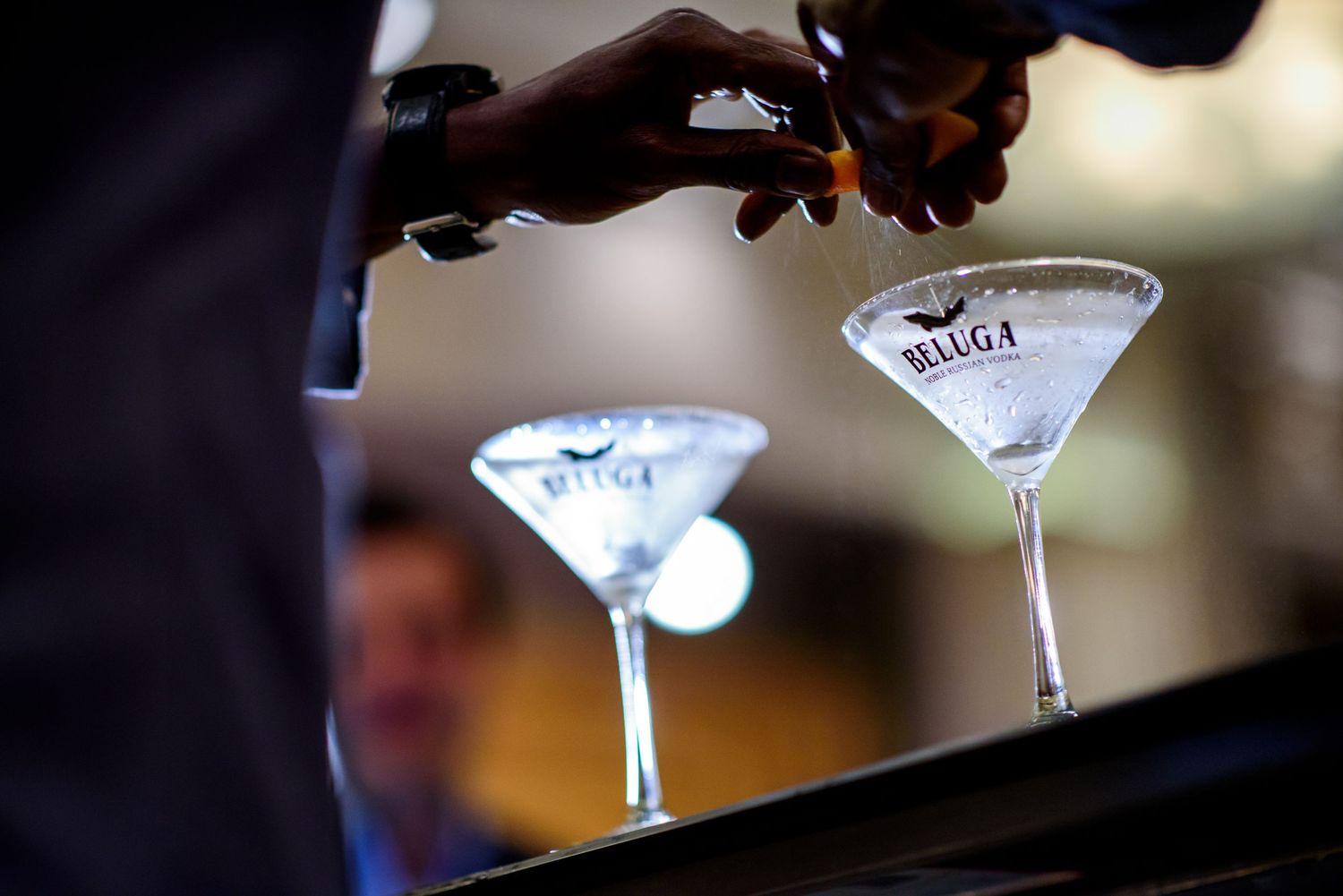 Bartender pouring two martinis into elegant cocktail glasses with precise technique.
