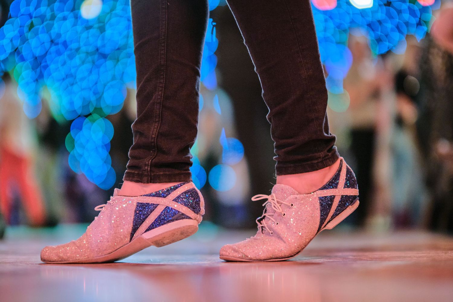 Close-up view of dancing feet in pink shoes on a lit dance floor.