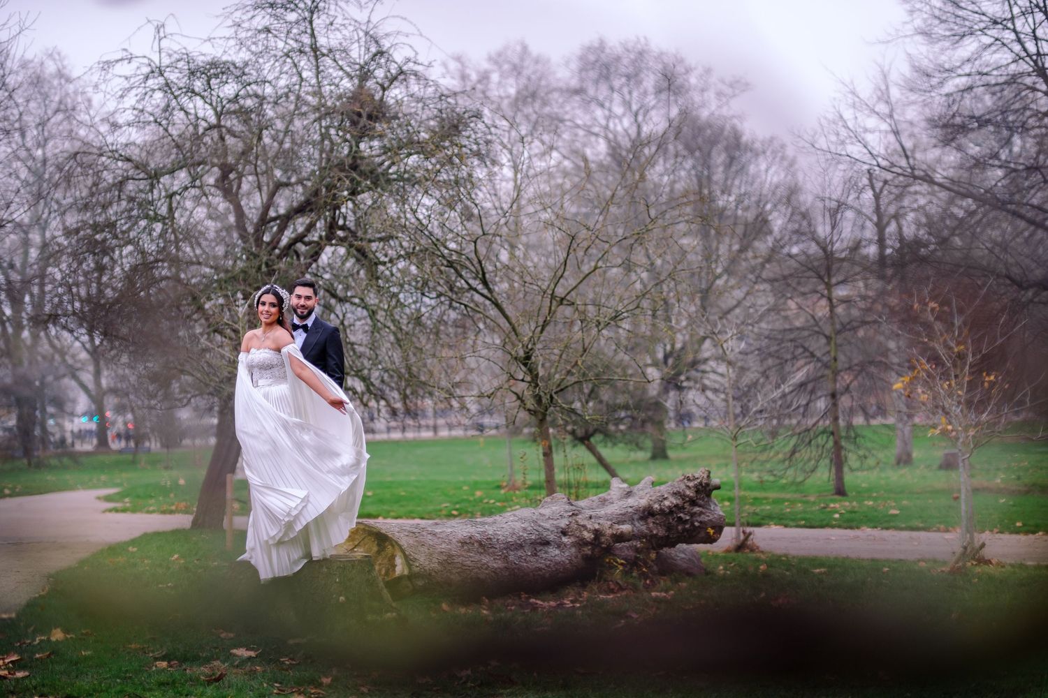 A couple poses near blooming cherry blossom trees in a spring garden during an outdoor photoshoot.